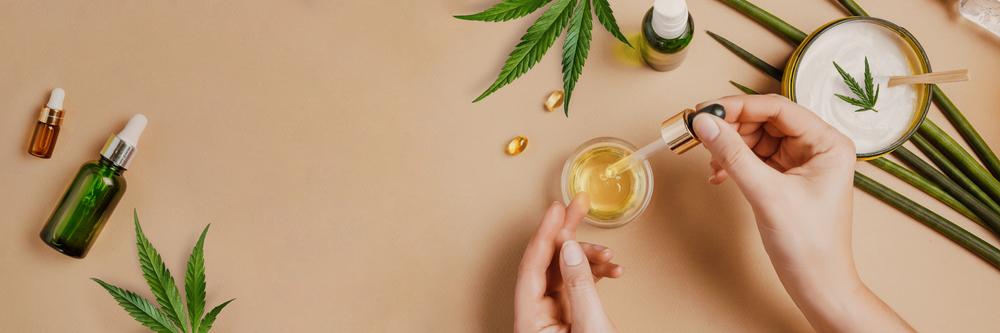 Pipette with CBD cosmetic oil in female hands on a table background with cosmetics